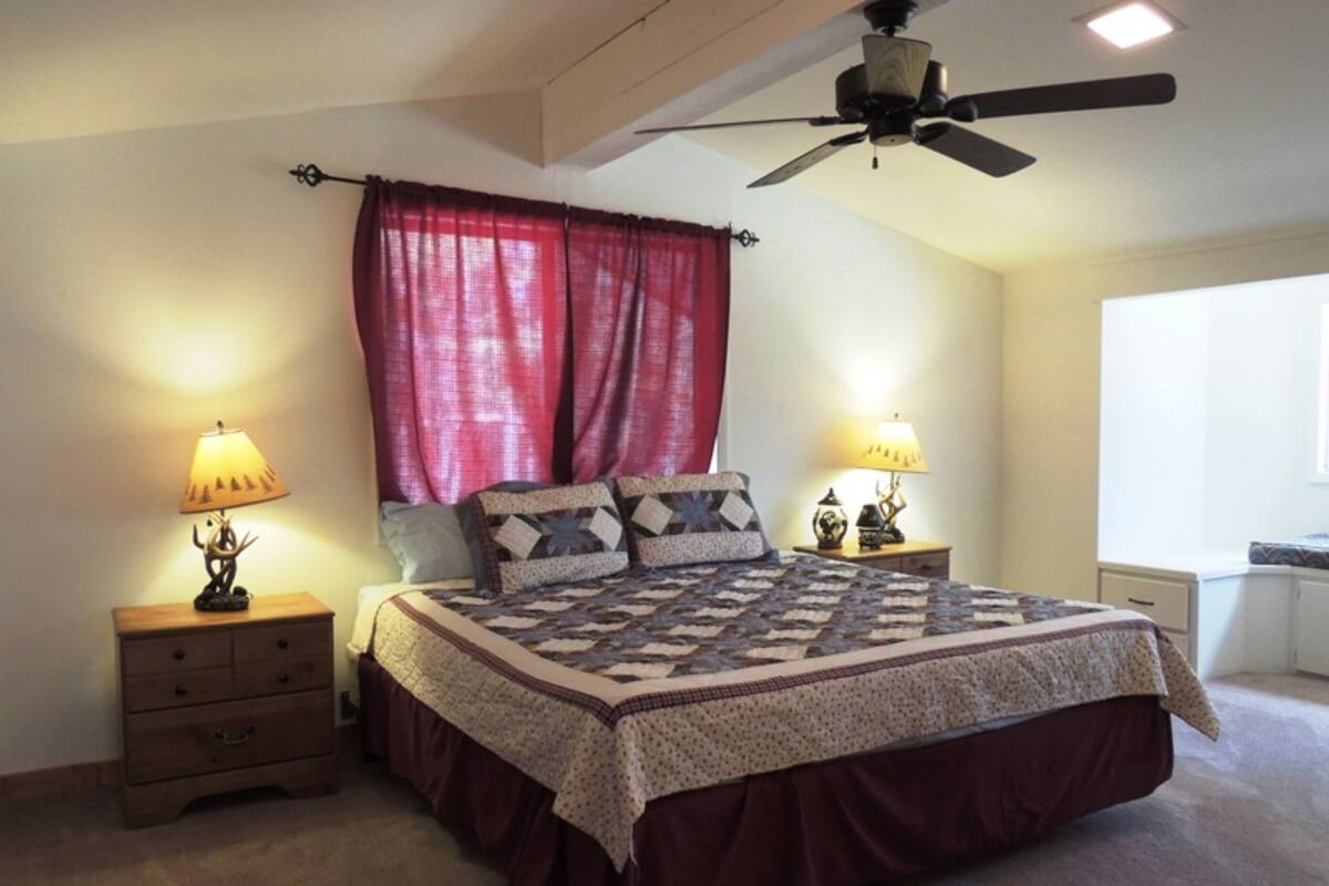 A bedroom with a bed, two bedside tables with lamps, a ceiling fan, and a window with curtains.