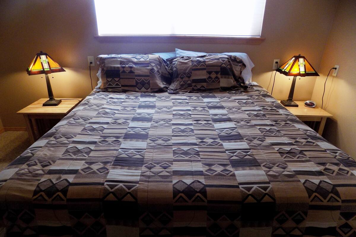 A bedroom with a large bed, two bedside lamps, and a window above the bed.