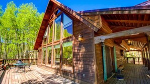 A wooden cabin with large windows, a deck, and a covered porch. - Country Club Homes (Angel Fire)
