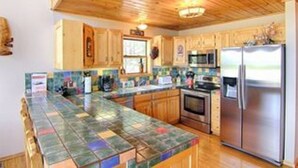 A kitchen with wooden cabinets, a tiled backsplash, stainless steel appliances, and a bar area. - Country Club Homes (Angel Fire)