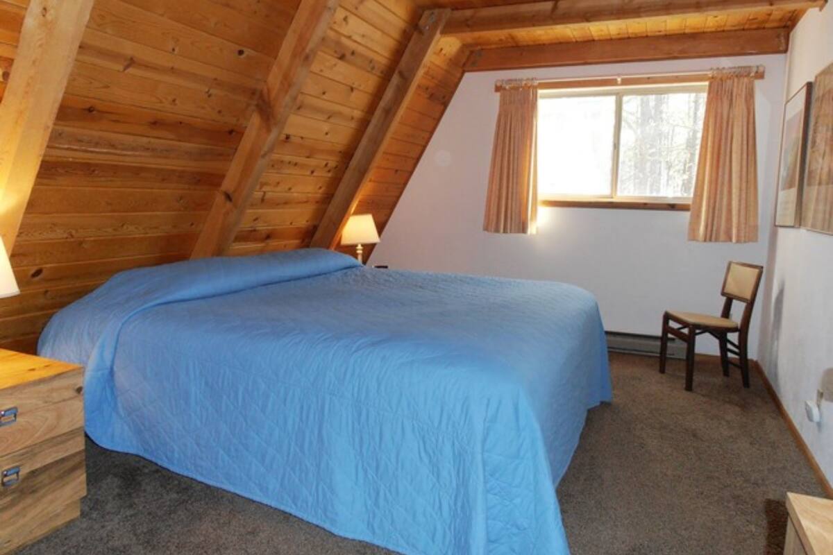 A bedroom with a sloped ceiling, a bed, a chair, and a window with curtains.