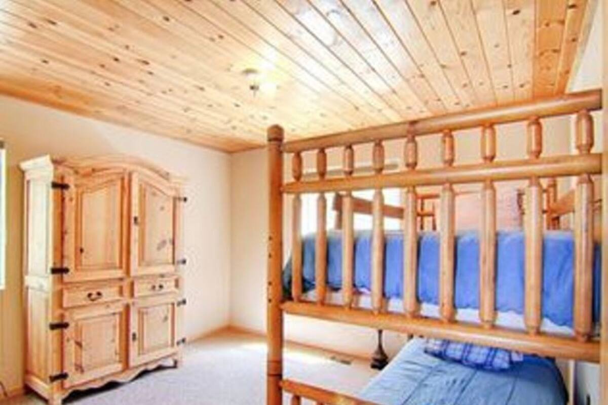 A room with a wooden ceiling, a bed with a blue bedspread, and a wooden wardrobe.