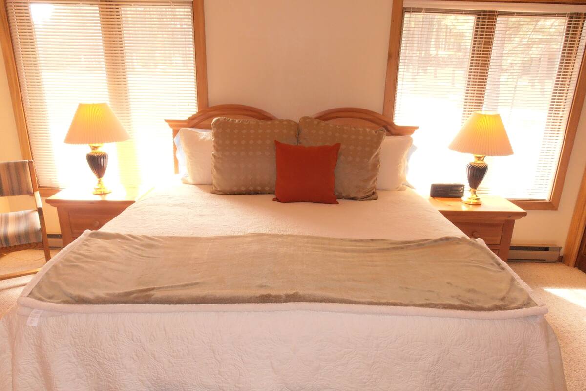 A neatly made bed with a white duvet, multiple pillows, and a bedside table with a lamp.