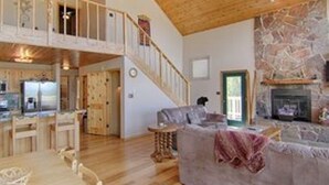 A spacious living area with a stone fireplace, wooden ceiling, and a cozy seating area. - Country Club Homes (Angel Fire)