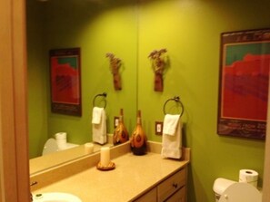 A bathroom with a green wall, a beige countertop, a sink, a toilet, and a mirror. - Mountain Haven (Angel Fire)