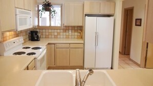 A compact kitchen with a white stove, a sink, and a refrigerator. - Mountain Haven (Angel Fire)