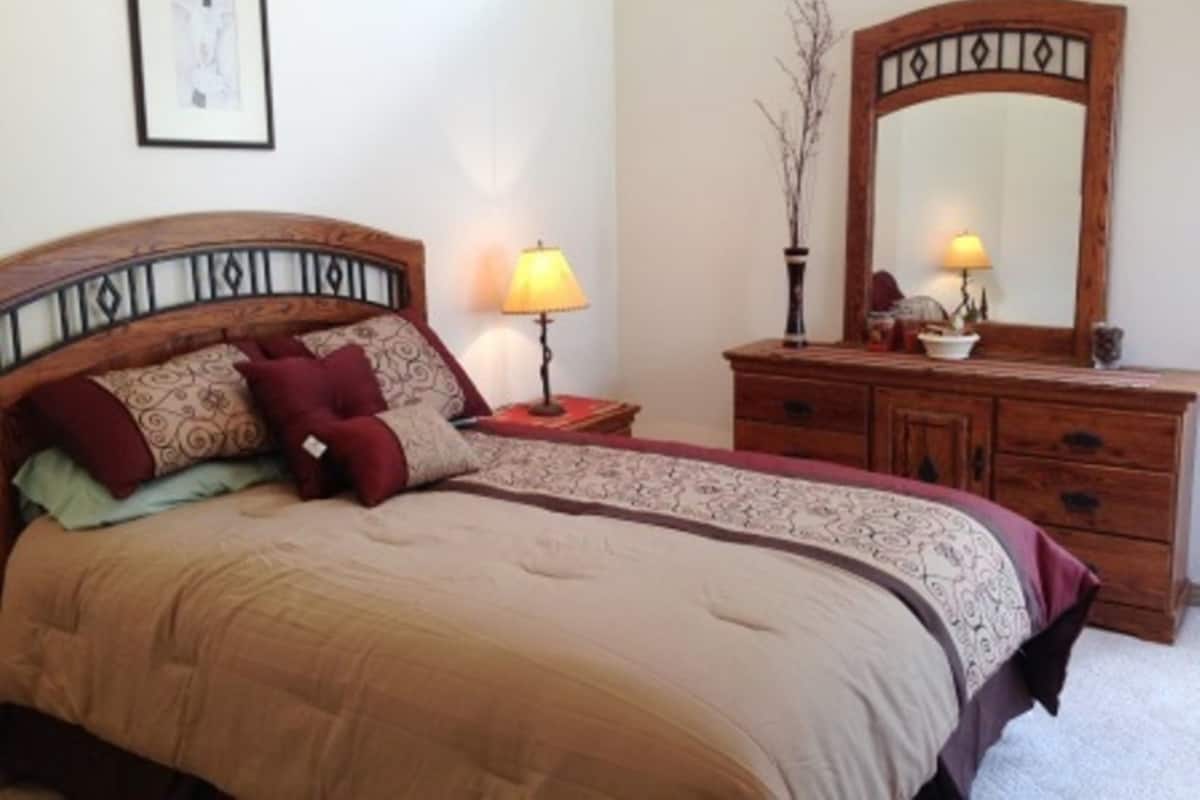 A bedroom with a bed, a dresser, two lamps, and a mirror.