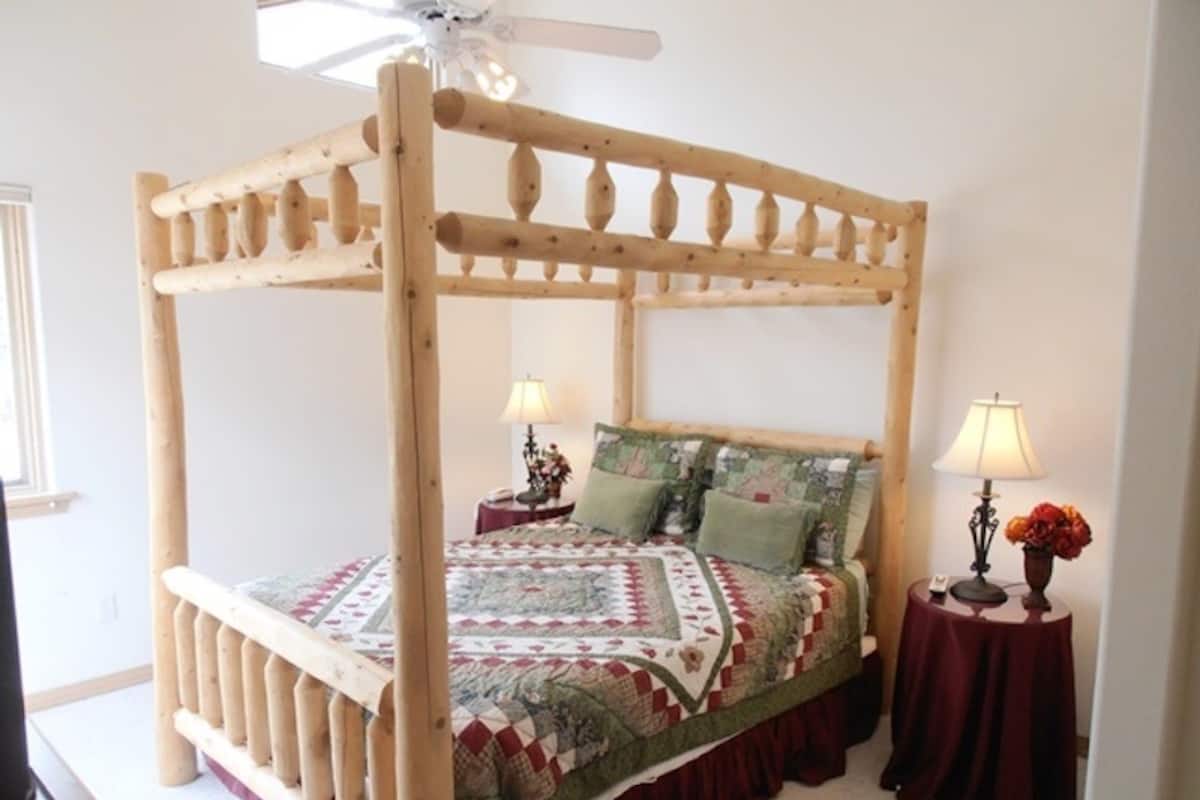 A four-poster bed with a quilt, two bedside tables with lamps, and a ceiling fan.