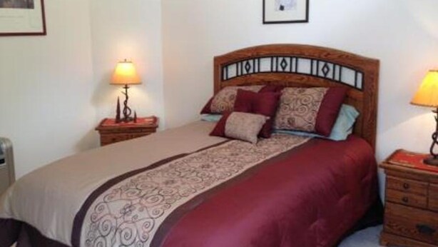 A neatly made bed with a patterned bedspread, two bedside tables with lamps, and a framed picture on the wall. - Mountain Haven (Angel Fire)