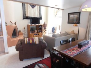 A living room with a sofa, a coffee table, a TV, and a dining area with chairs and a table. - Mountain Haven (Angel Fire)