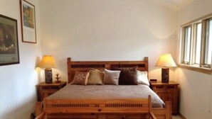 A bedroom with a wooden bed, two bedside tables with lamps, a window, and a framed picture on the wall. - Mountain Haven (Angel Fire)