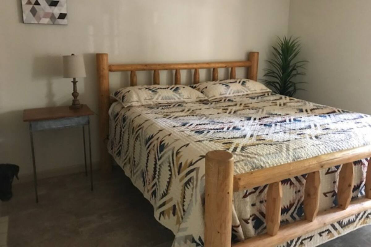 A bedroom with a wooden bed frame, patterned bedding, a small bedside table with a lamp, and a wall-mounted artwork.