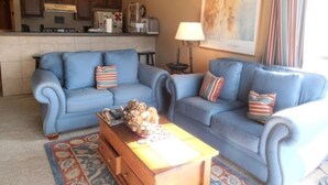 A living room with two blue sofas, a wooden coffee table, and a patterned rug. - Mountain Meadows (Angel Fire)