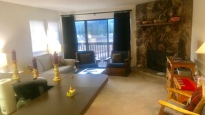 A living room with a fireplace, a dining table, and a view of the outdoors. - Mountain Meadows (Angel Fire)