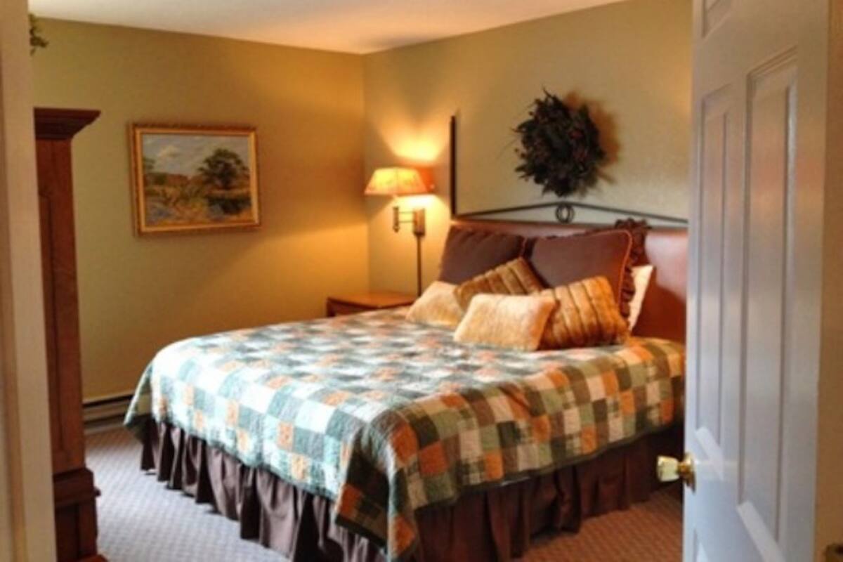 A bedroom with a bed, a nightstand, a lamp, a painting on the wall, and a door.