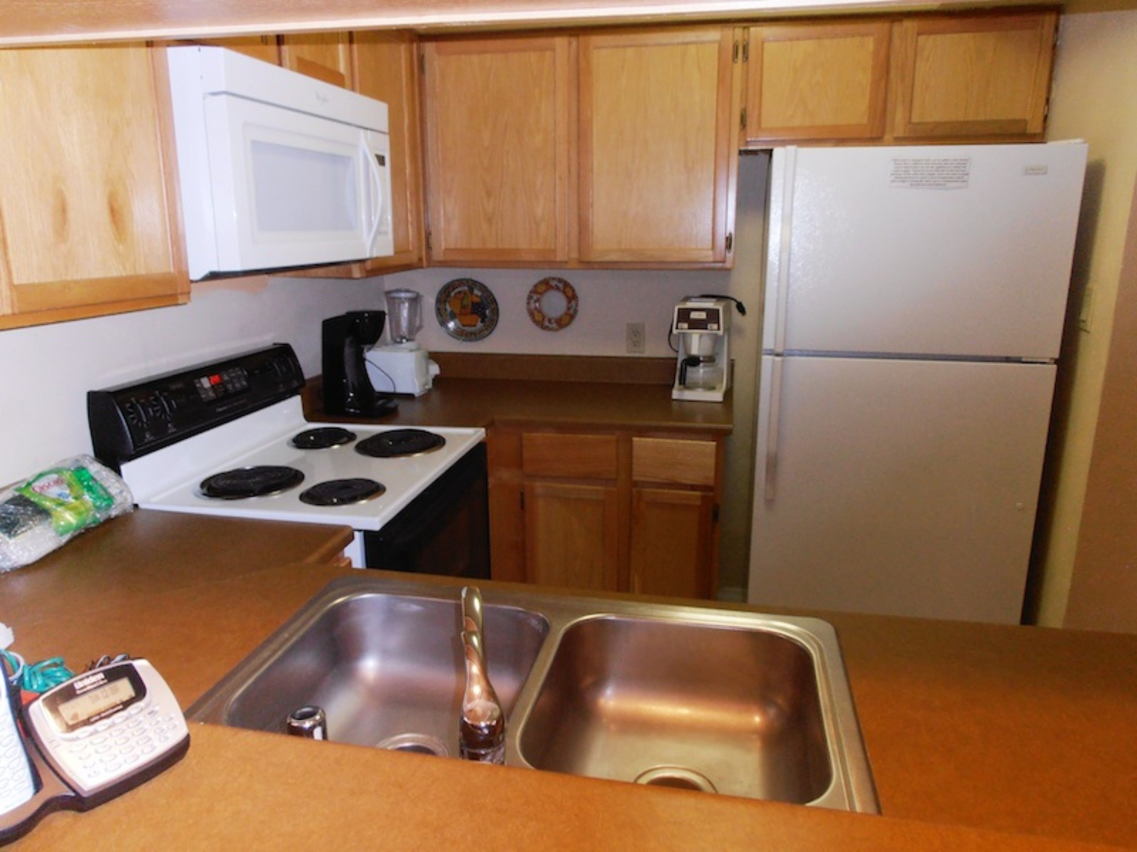 A kitchen with wooden cabinets, a white stove, a sink, a coffee maker, and a refrigerator.