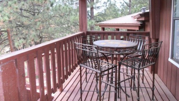 Een houten terras met een ronde tafel en stoelen, omringd door een houten hek, met uitzicht op een bebost gebied.