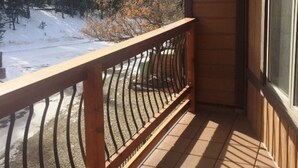 A wooden balcony with a metal railing overlooking a snowy landscape with trees and hills. - Ski Run (Angel Fire)