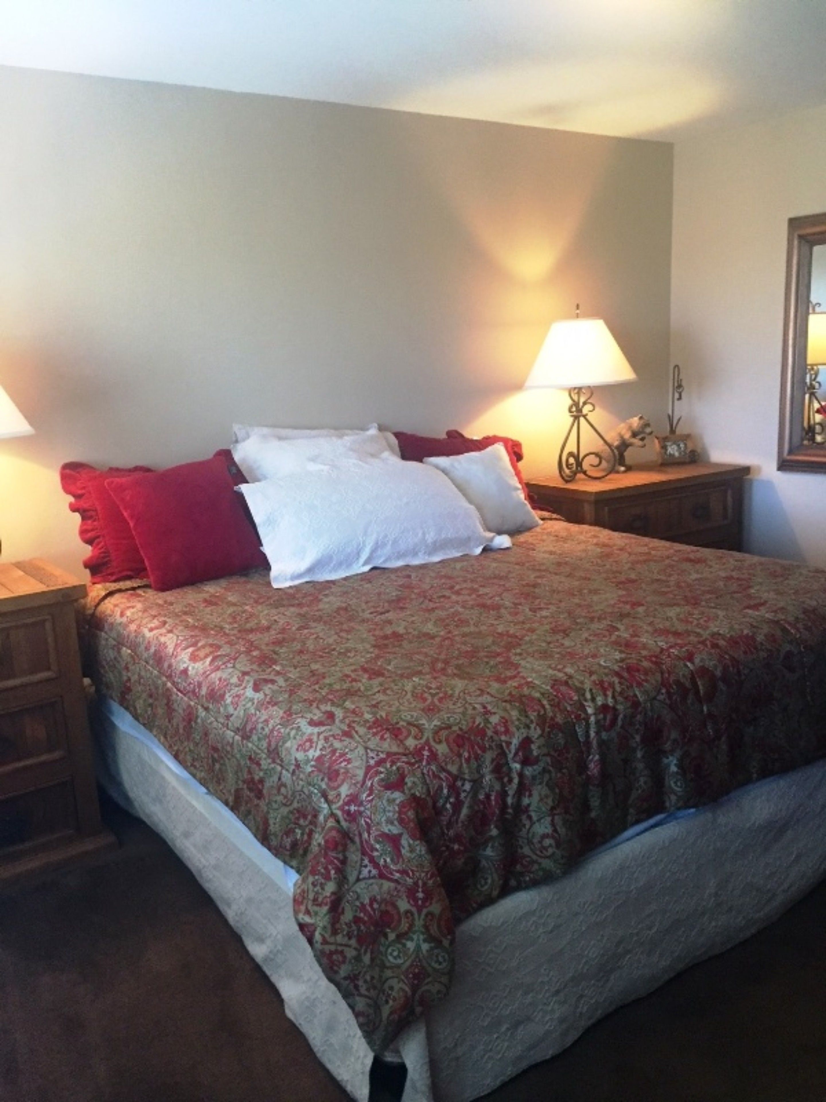 A neatly made bed with a floral bedspread, two bedside tables with lamps, and a nightstand with a decorative item.
