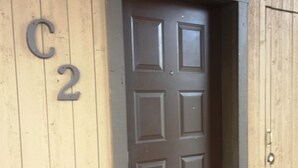 A wooden door with a dark brown panel, a metal number 'C2' sign, and a metal doorknob. - Ski Run (Angel Fire)