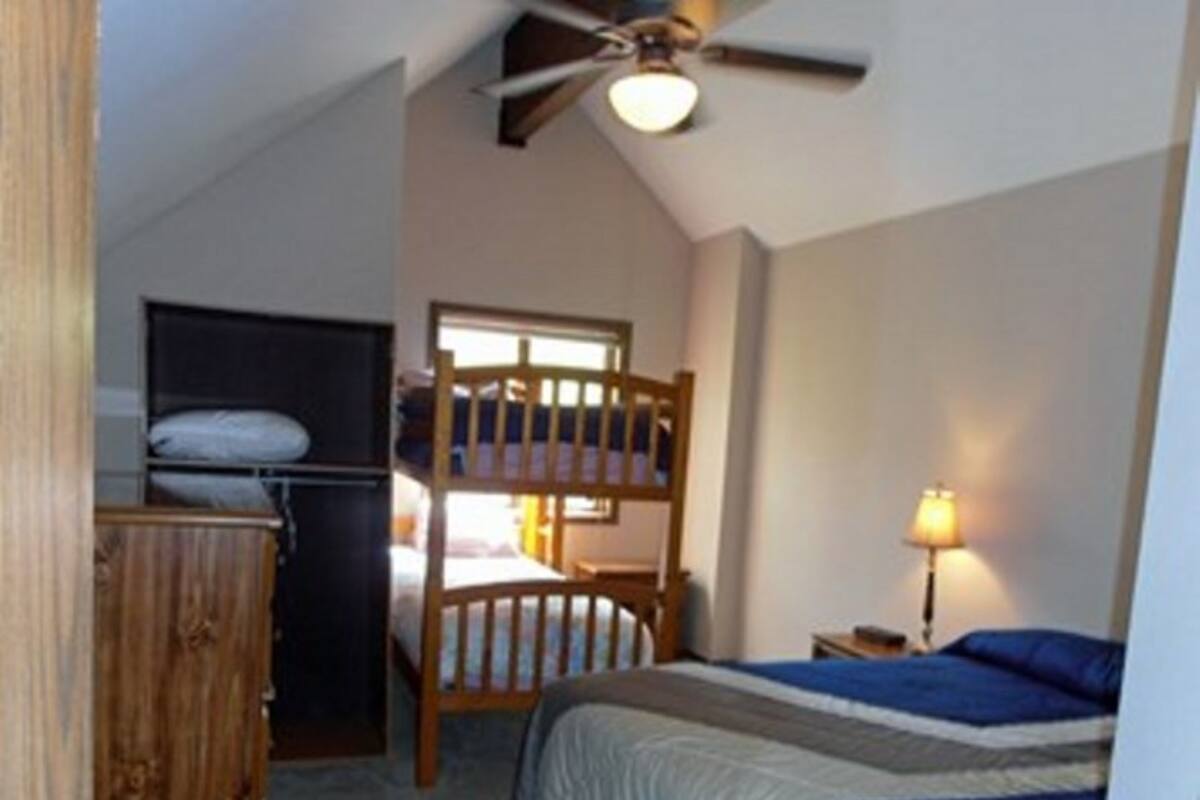A bedroom with bunk beds, a ceiling fan, a bedside lamp, and a dresser.