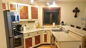 Een functionele keuken met een koelkast, fornuis, magnetron en spoelbak. Het heeft decoratieve kastjes en een raam met gordijnen.