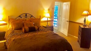 Een slaapkamer met een bed, twee bedlampen, een nachtkastje en een deur naar een andere kamer.