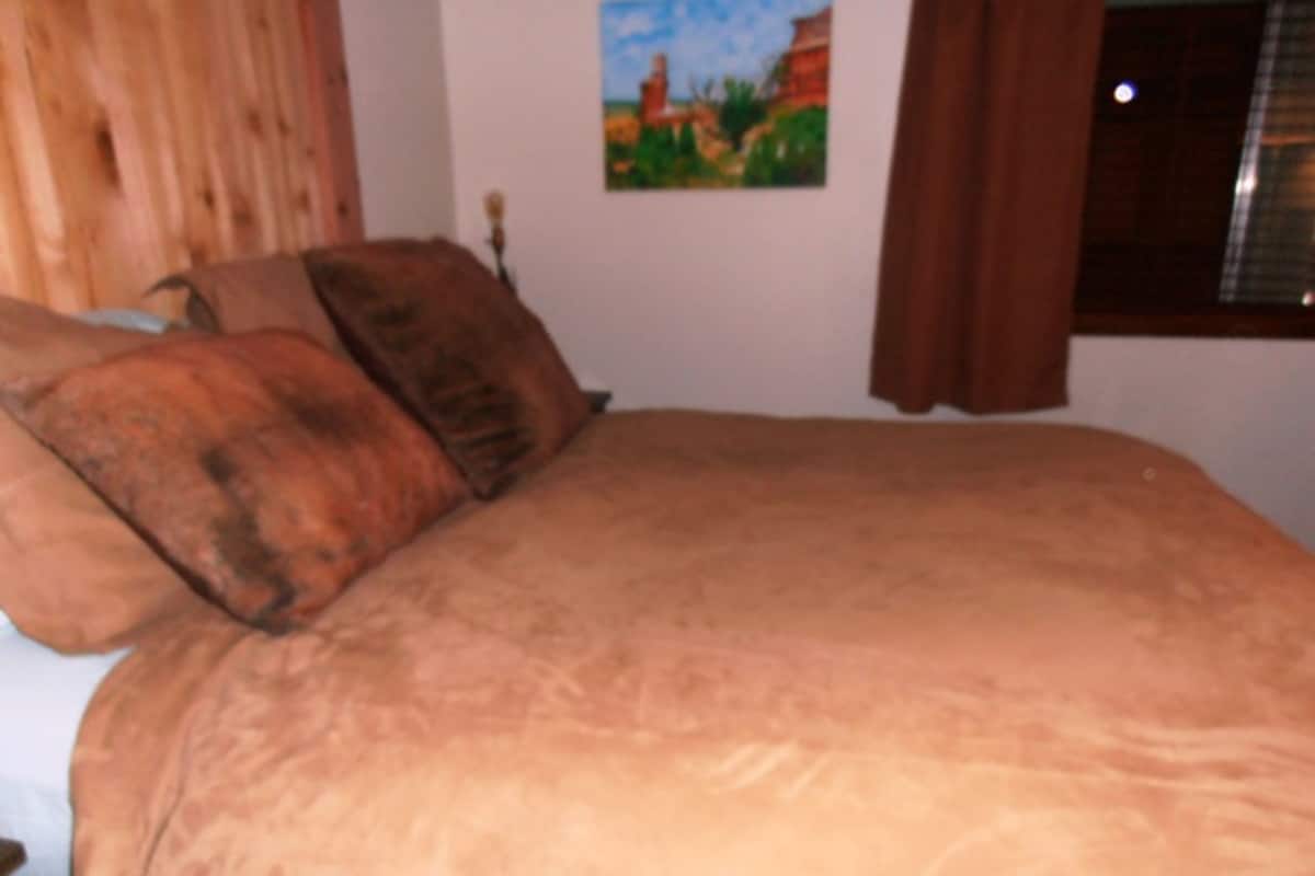 A bedroom with a large bed, two pillows, a painting on the wall, and a window with curtains.
