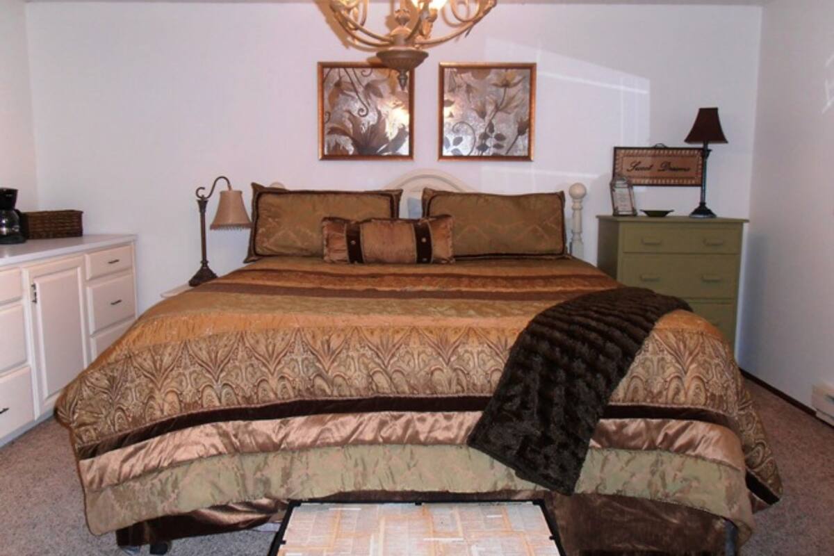 A bedroom with a large bed, a dresser, a nightstand, and a chandelier.