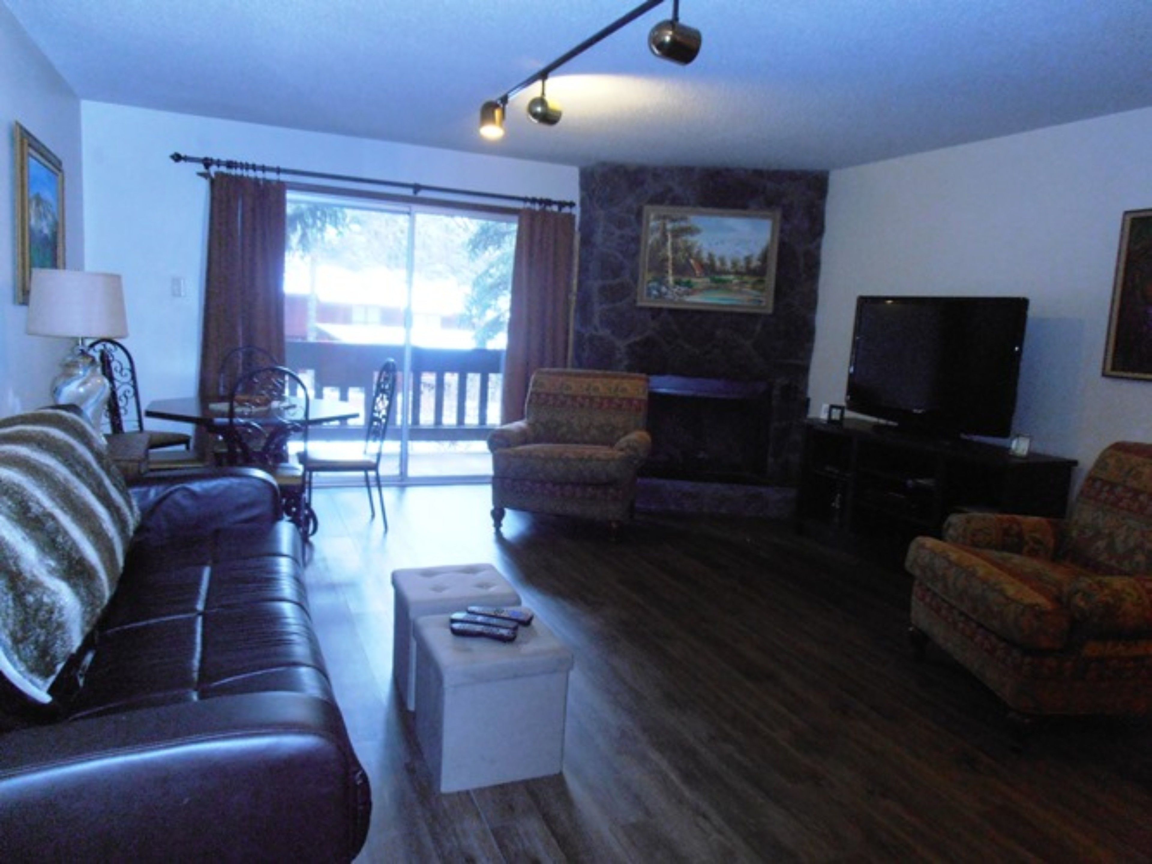 A living room with a sofa, armchairs, a fireplace, a television, and a balcony with curtains.