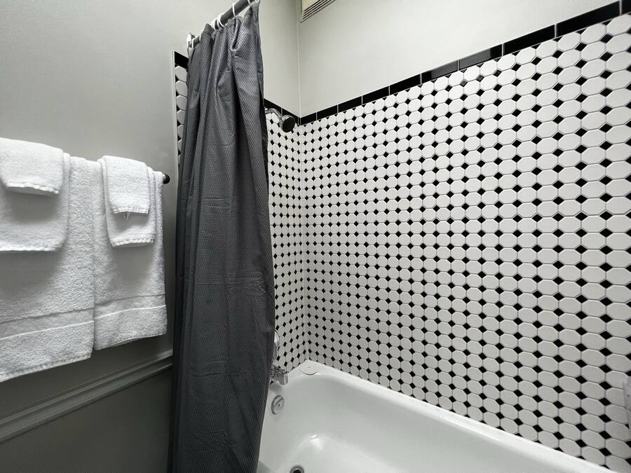 A bathroom with a bathtub, a shower curtain, and a tiled wall with a geometric pattern.