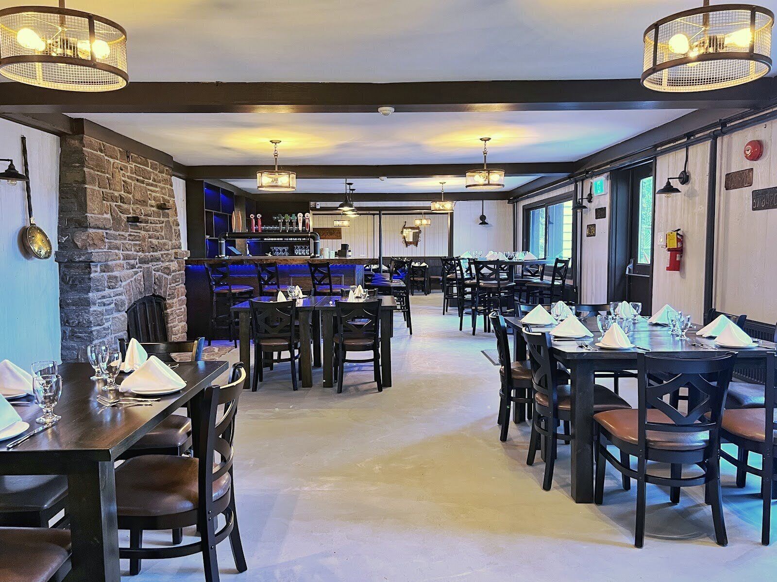 Un restaurant doté de nombreuses tables et chaises, d’un mur en pierre et de luminaires suspendus.