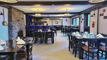 En restaurang med flera bord och stolar, en vägg av sten och hängande lampor.