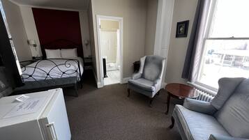 A hotel room with a bed, a grey armchair, a small table, and a window with a view of buildings.