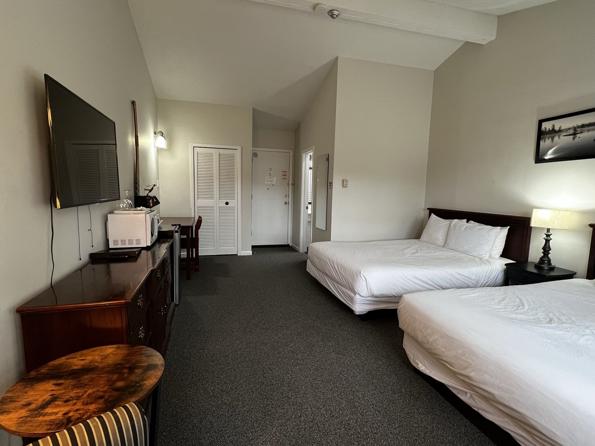 A hotel room with two beds, a desk with a computer, a TV, and a small seating area.