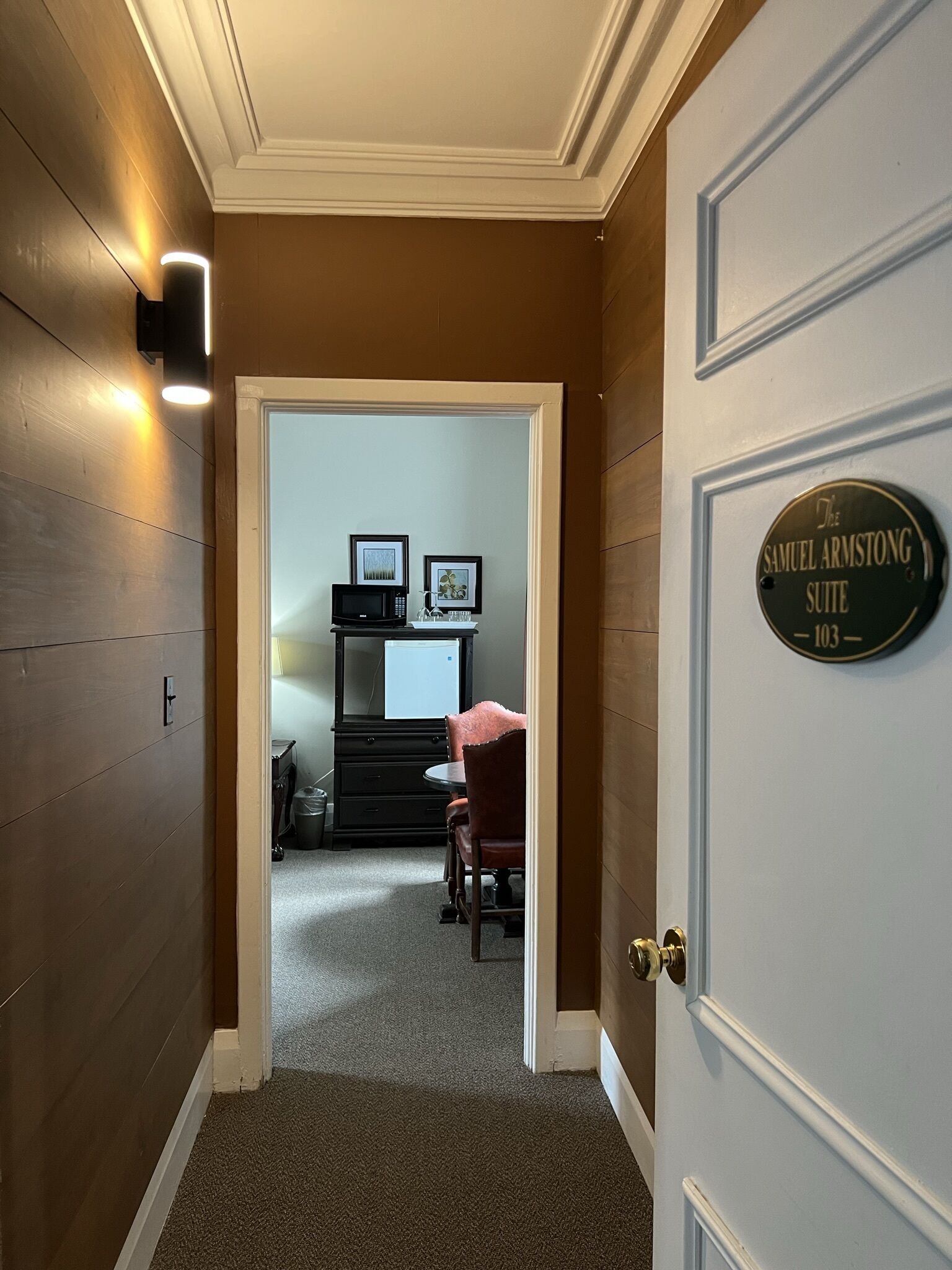 Un pasillo que conduce a una habitación con un letrero que dice 'The Samuel Armstrong Suite 103'.