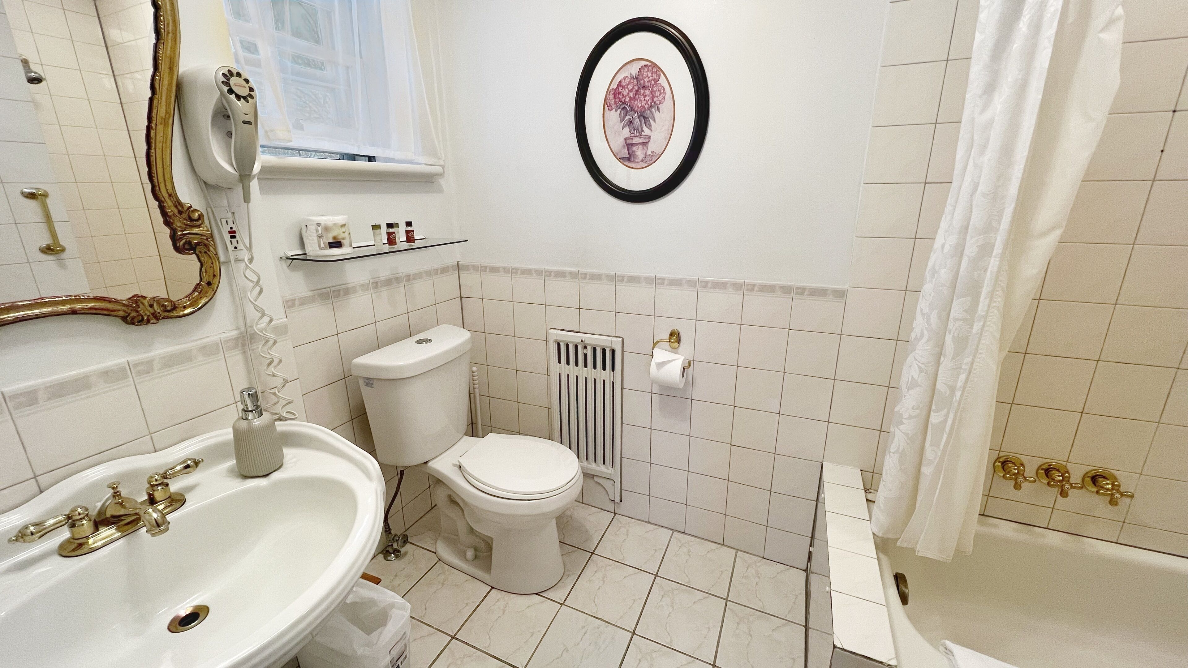 A bathroom with a white sink, toilet, and bathtub. There is a framed picture on the wall and a window with a curtain.