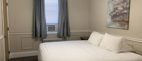 A bedroom with a large bed, a radiator, a window with curtains, and a painting on the wall.
