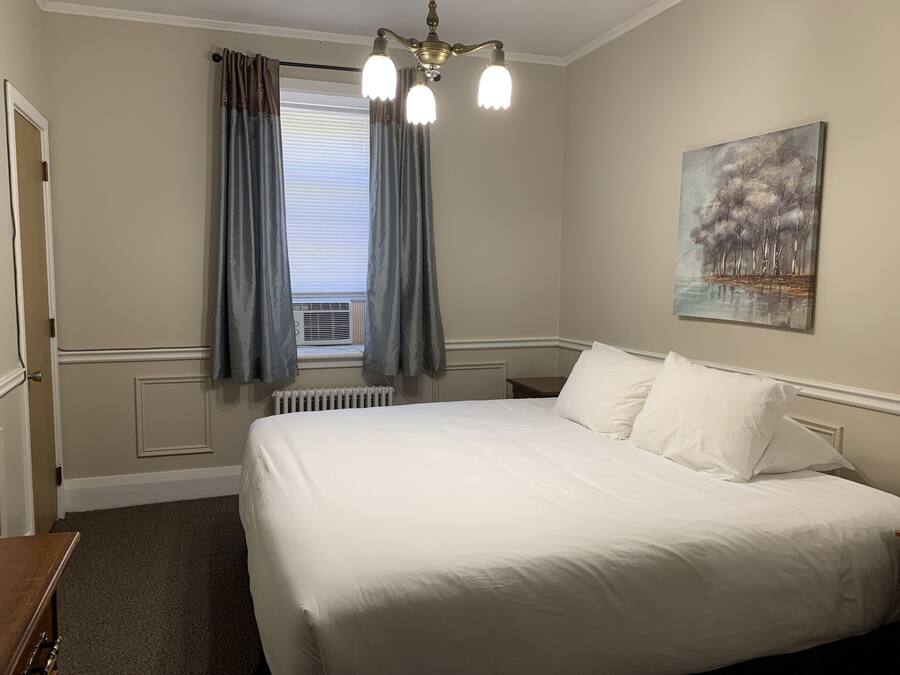 A bedroom with a large bed, a radiator, a window with curtains, and a painting on the wall.