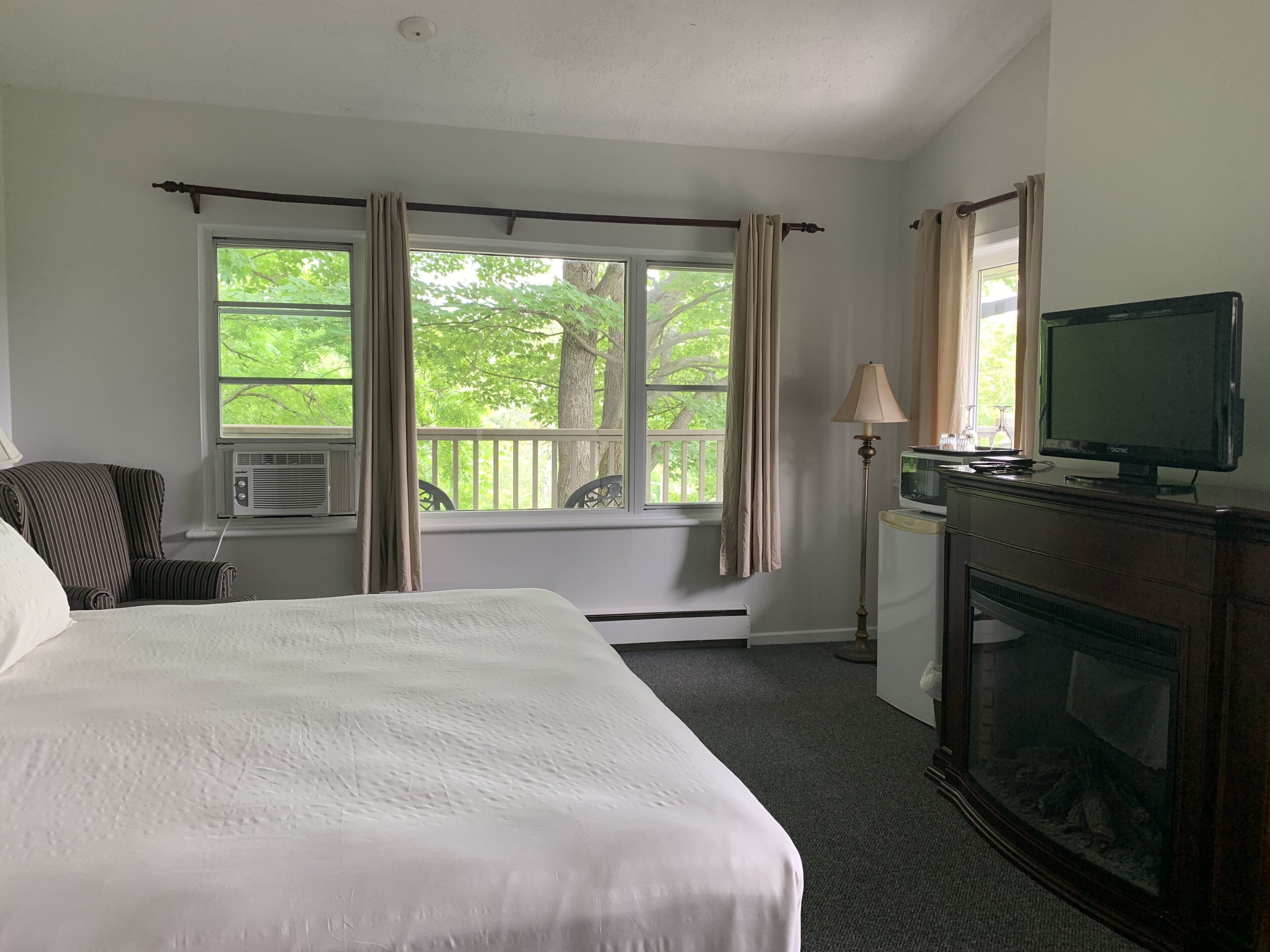 Una habitación de hotel con una cama, televisión, chimenea, escritorio con silla y ventana con cortinas.