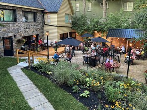An outdoor patio area with tables and chairs, surrounded by a garden with various plants and flowers. - Inn at the Falls (Bracebridge)