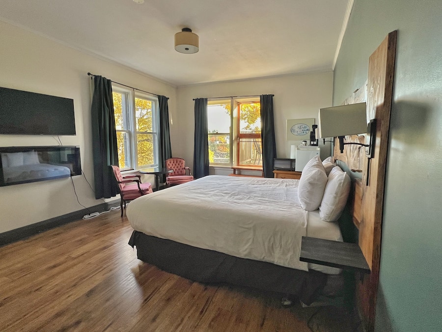 Une chambre d’hôtel avec un grand lit, un téléviseur fixé au mur, un bureau avec une chaise et un balcon avec des rideaux.