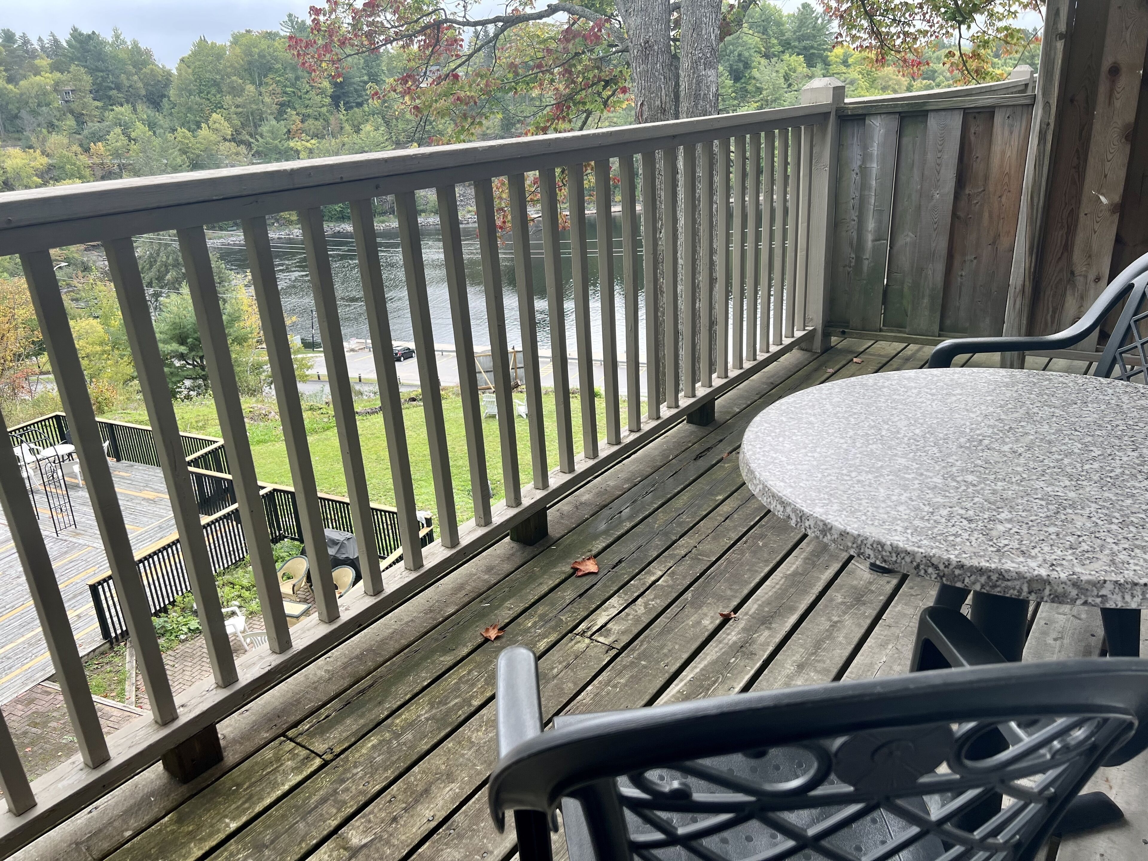 En træterrasse med et stensæt af borde og stole, med udsigt over vand og en parkeringsplads.