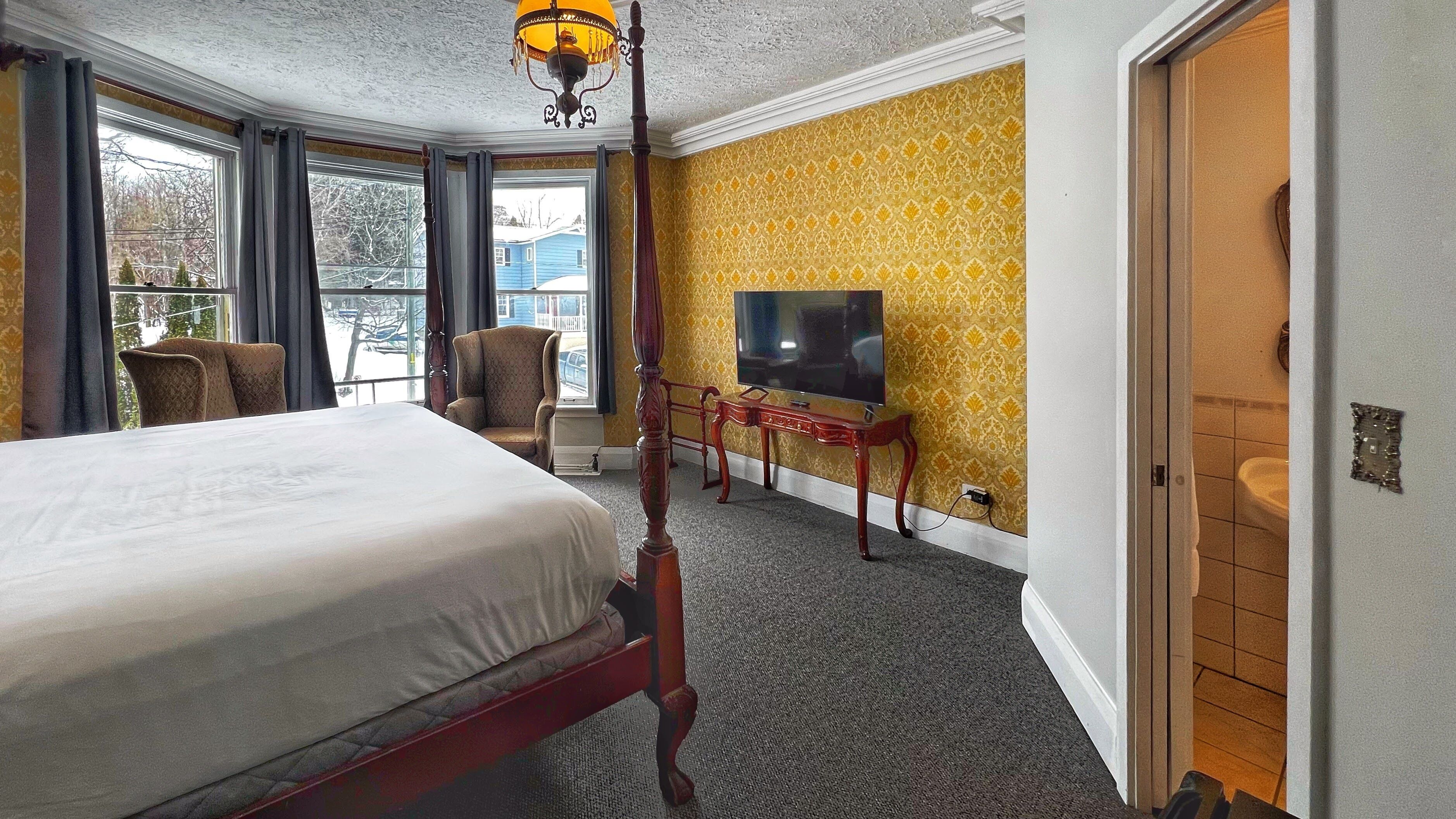 A hotel room with a four-poster bed, a television, a chair, and a view of the outside.