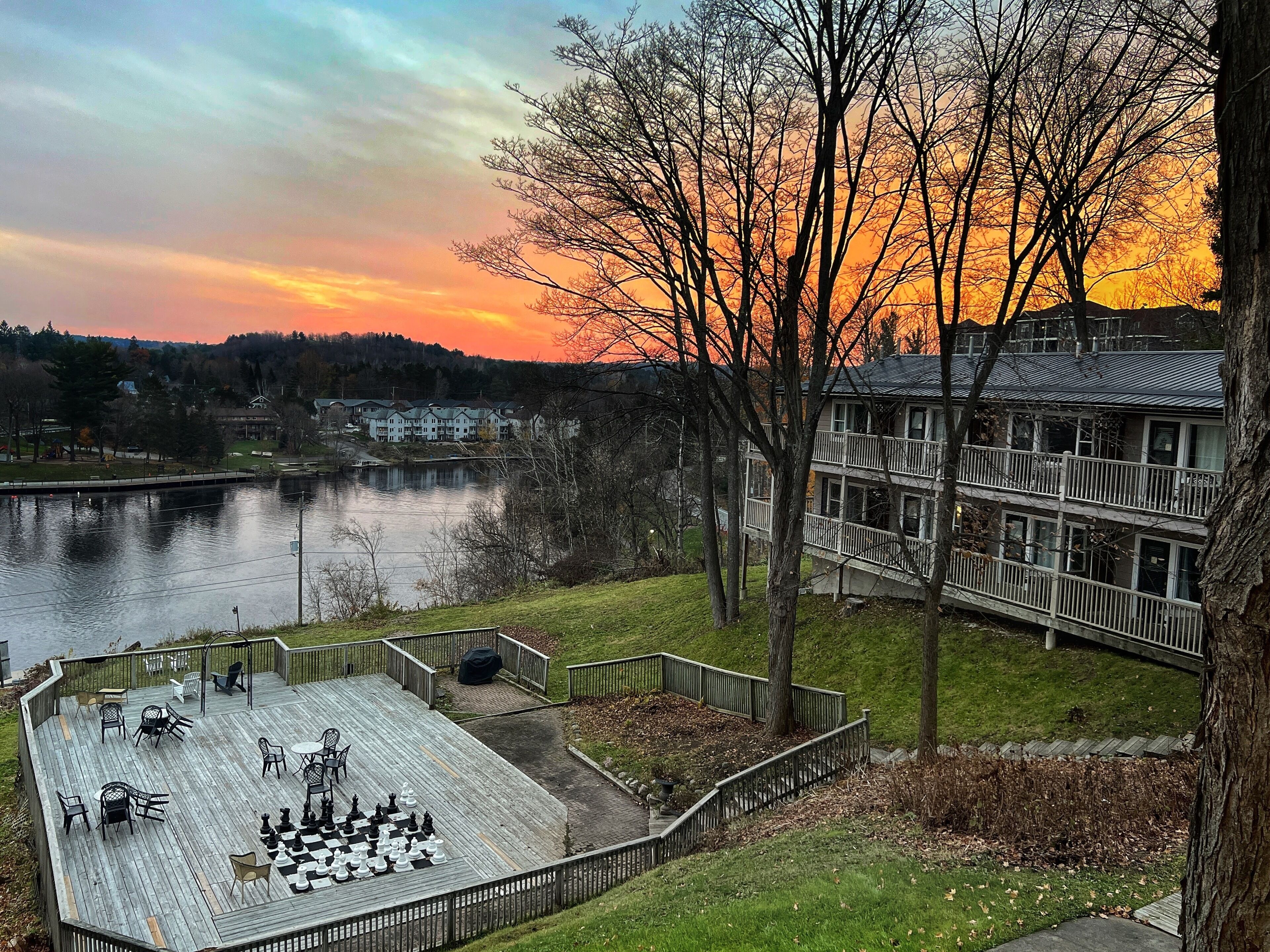 A deck with chess set, a lake, and buildings in the background.