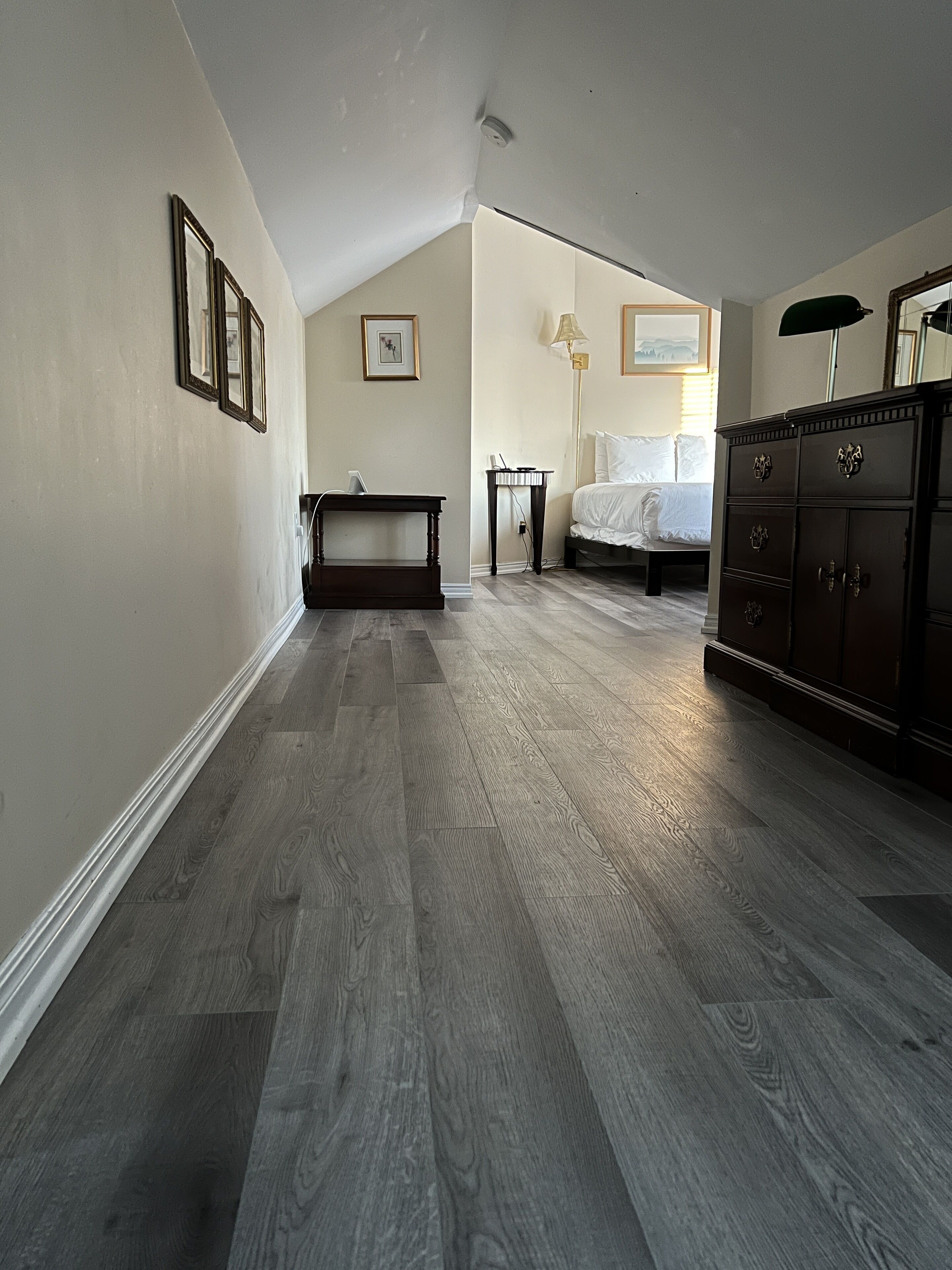 Une pièce avec un plafond en pente, un plancher en bois, un lit, une commode et des tableaux encadrés accrochés au mur.