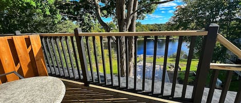 A wooden deck with a table and chairs, overlooking a body of water and a grassy area.