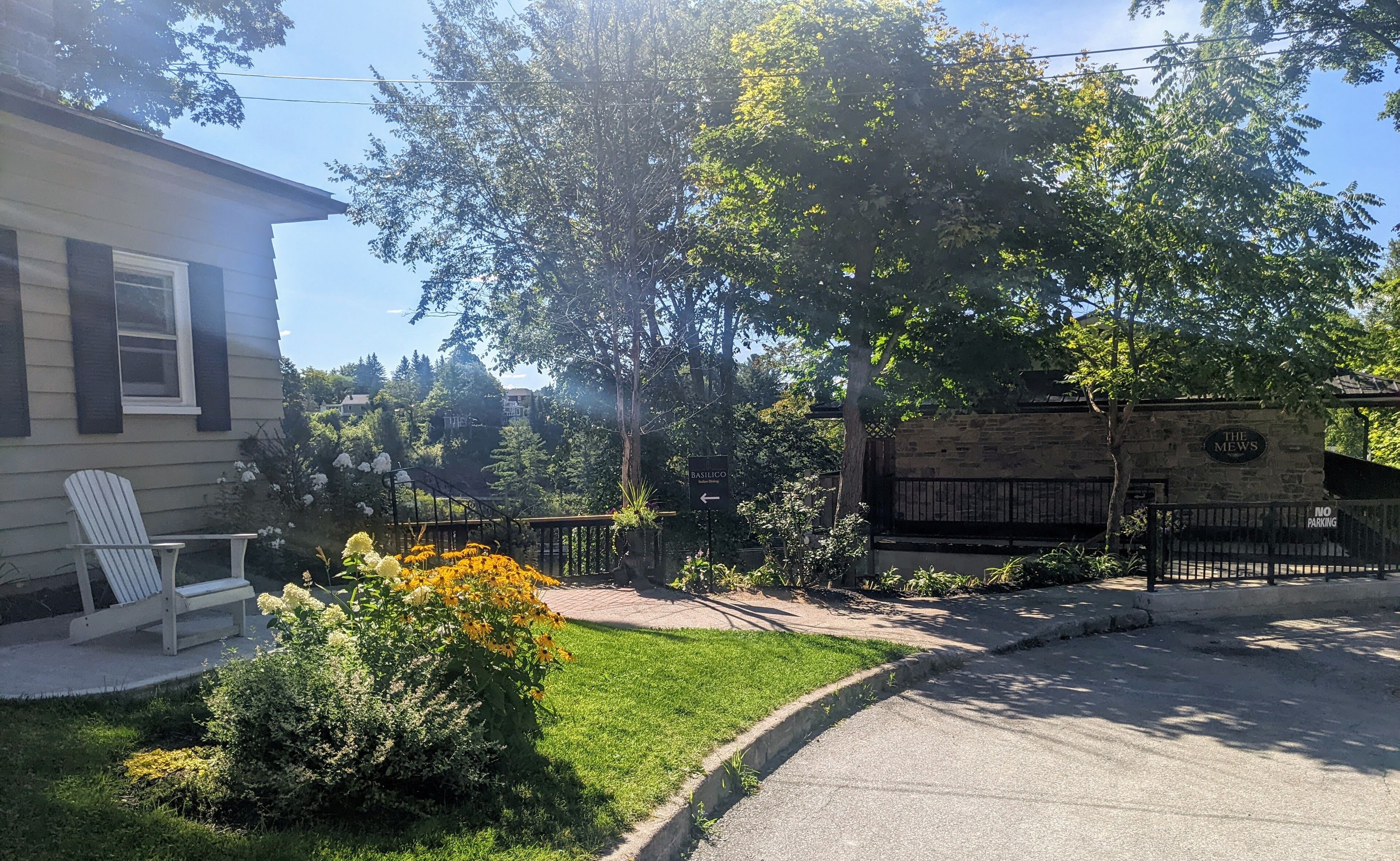 A residential area with a house, a white chair, and a garden with various plants and flowers.