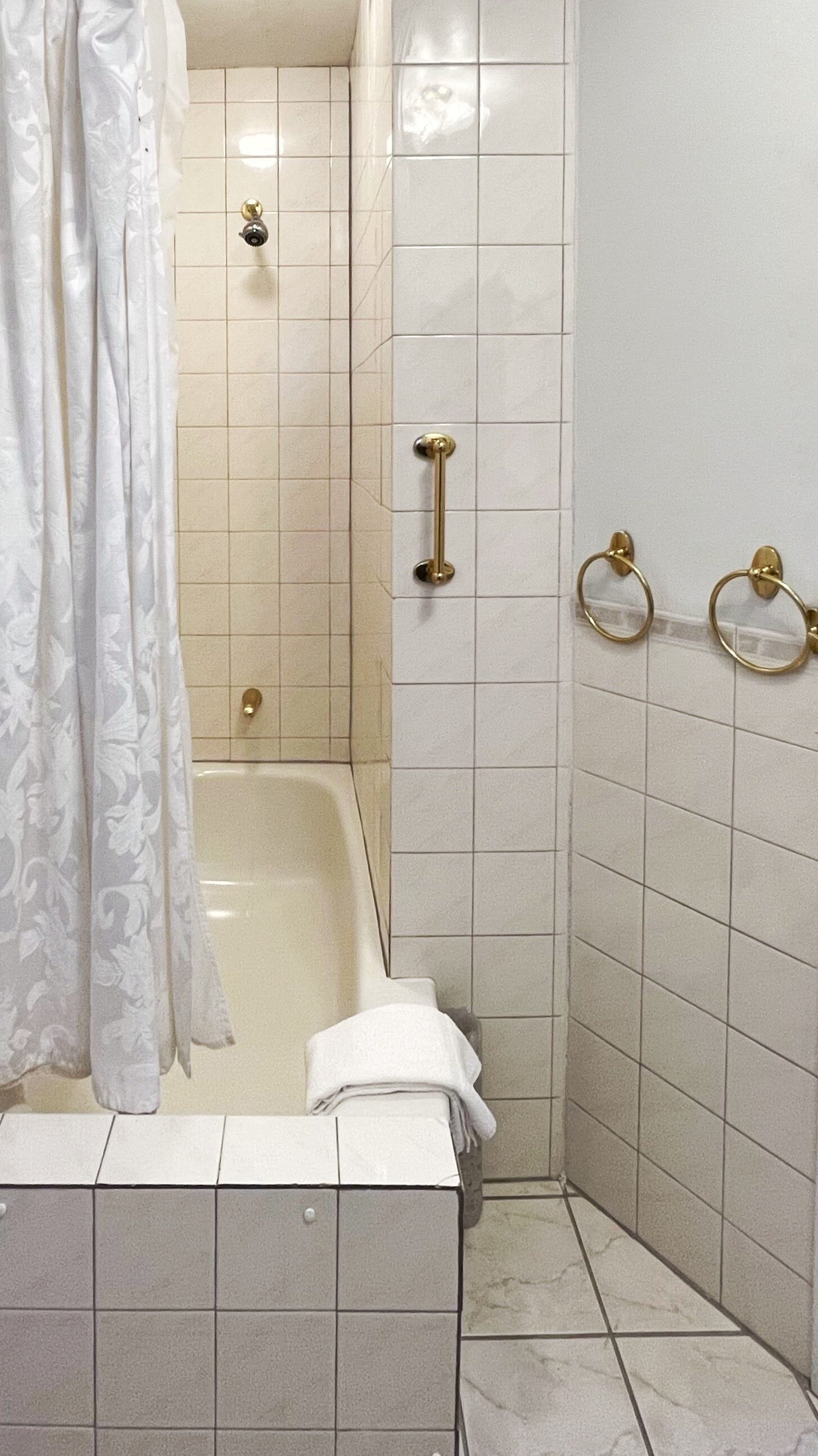 A bathroom with a bathtub, a shower, and a toilet. There are grab bars and a towel rack.
