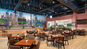A restaurant with a cityscape mural, multiple tables and chairs, a bar area, and sports screens. - Impressive Premium Punta Cana (Punta Cana)